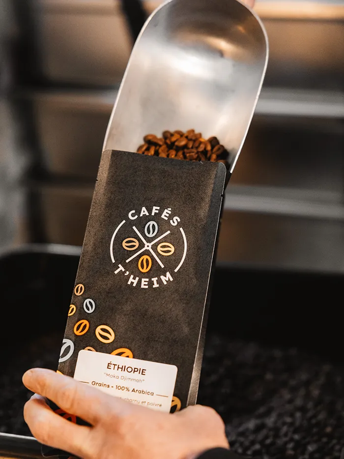 Personne versant des grains dans un paquet de café Cafés T'heim