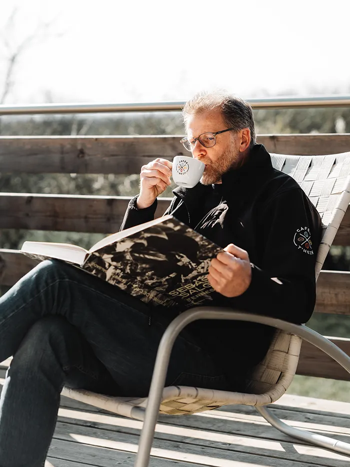 Régis buvant un café sur une chaise en extérieur en soleil